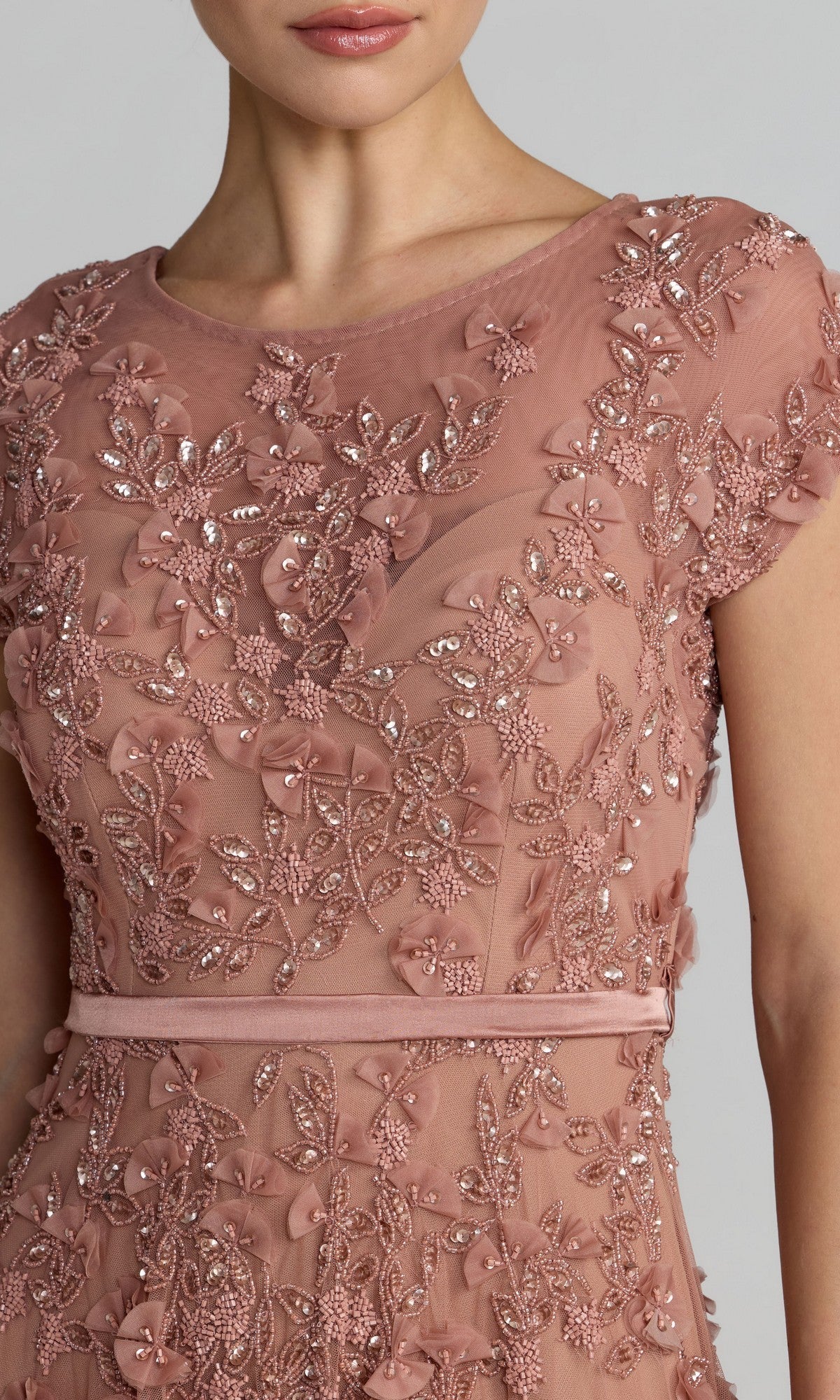 A woman wears the Mac Duggal 94339 midi wedding guest dress, featuring dusty pink fabric, floral embroidery, sequins, cap sleeves, and a thin waist belt—ideal for a charming wedding reception look.